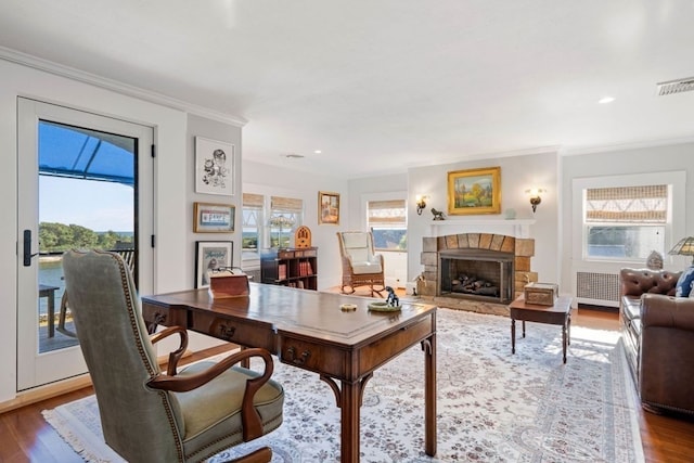 office area with a fireplace, ornamental molding, a healthy amount of sunlight, and wood-type flooring