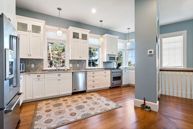 kitchen featuring premium appliances, tasteful backsplash, decorative light fixtures, and white cabinetry