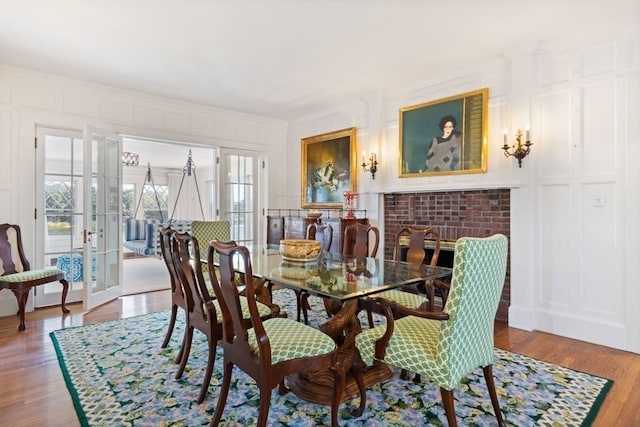 dining room featuring french doors, a brick fireplace, ornamental molding, and wood-type flooring