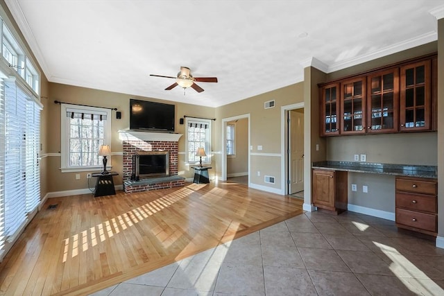 unfurnished living room featuring a brick fireplace, baseboards, built in desk, and ornamental molding