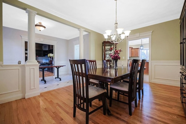 dining space featuring light wood finished floors, a chandelier, wainscoting, and ornate columns