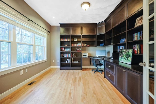 office space featuring visible vents, baseboards, light wood-style flooring, and built in desk