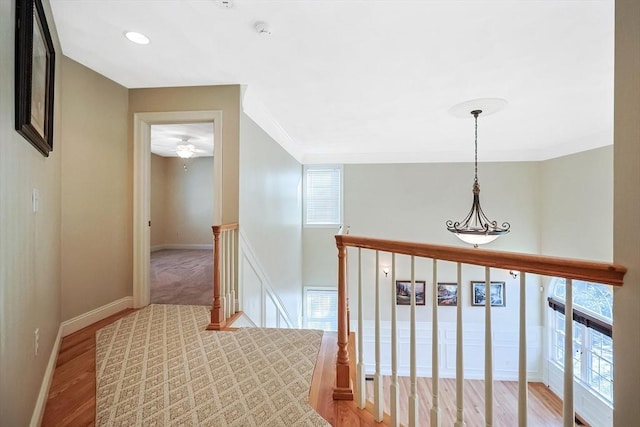 corridor with an upstairs landing, crown molding, light wood-type flooring, and baseboards