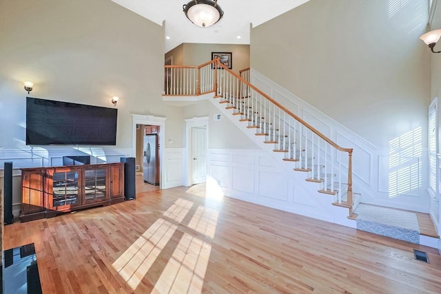 living room featuring visible vents, wood finished floors, stairway, a decorative wall, and a towering ceiling