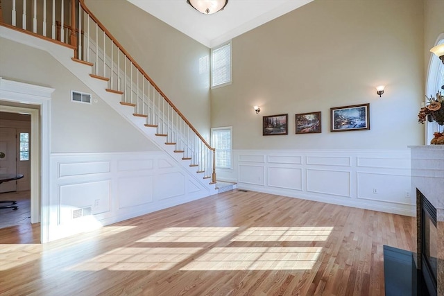 unfurnished living room featuring a glass covered fireplace, stairway, wood finished floors, and visible vents