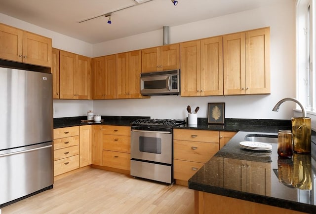 kitchen featuring stainless steel appliances, a sink, light wood-style flooring, and dark stone countertops