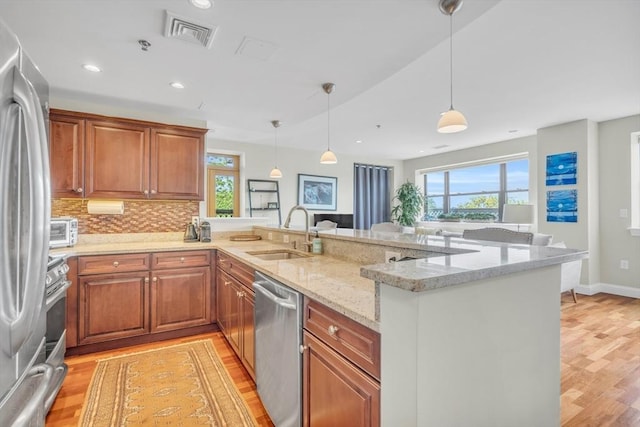 kitchen featuring visible vents, appliances with stainless steel finishes, brown cabinetry, a sink, and a peninsula