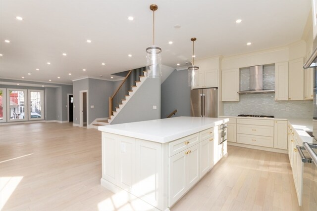 kitchen with tasteful backsplash, wall chimney range hood, a kitchen island, hanging light fixtures, and stainless steel appliances