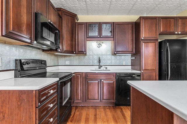 kitchen featuring an ornate ceiling, a sink, light countertops, black appliances, and glass insert cabinets