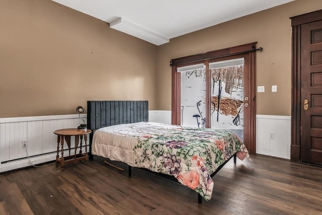 bedroom featuring access to exterior, baseboard heating, dark wood-style flooring, and wainscoting