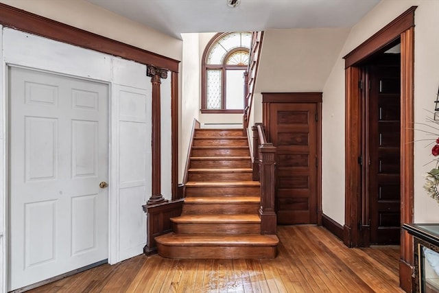 stairs featuring ornate columns, wood finished floors, and baseboards