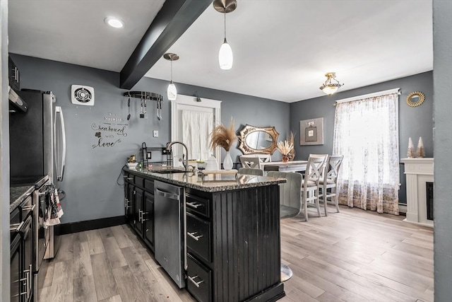 kitchen featuring dark cabinets, stainless steel appliances, a sink, dark stone counters, and pendant lighting