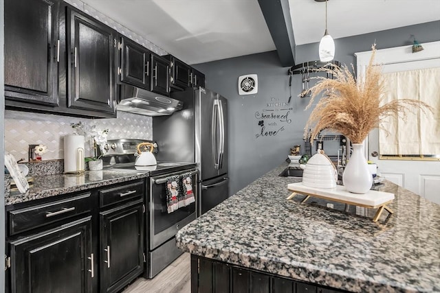 kitchen with pendant lighting, stainless steel appliances, dark stone counters, dark cabinetry, and under cabinet range hood