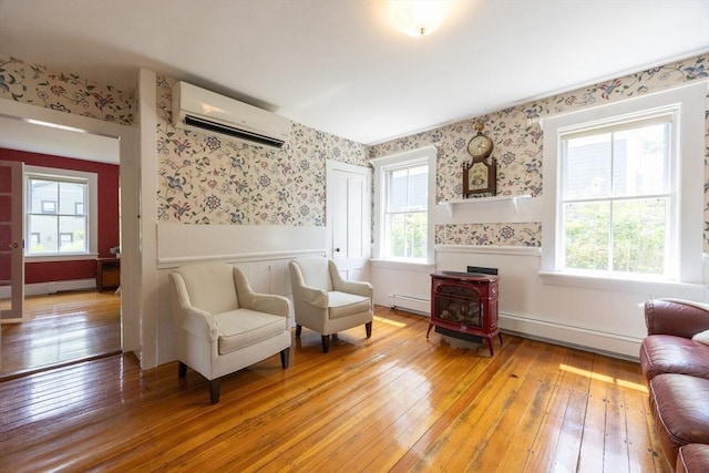 75 Union St, Holliston, MA 01746 - living area featuring a wall mounted air conditioner, baseboard heating, wallpapered walls, wainscoting, and a wood stove