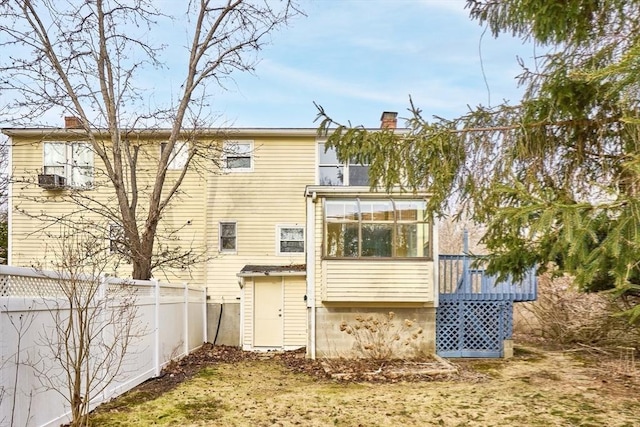 rear view of property featuring a deck, fence, a sunroom, and a chimney