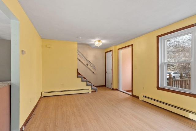 empty room with stairway, baseboards, light wood-type flooring, and a baseboard radiator