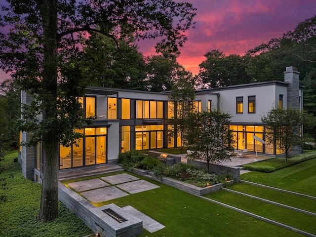 back house at dusk featuring a patio area and a lawn