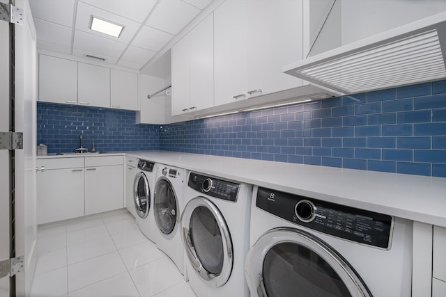 washroom featuring cabinets, sink, washing machine and dryer, and light tile floors