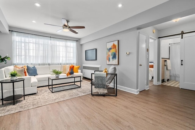 living room featuring radiator, wood-type flooring, a barn door, and ceiling fan