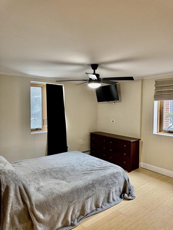 bedroom featuring light wood-style floors, crown molding, baseboards, and a ceiling fan