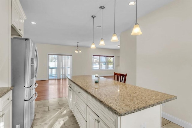 kitchen featuring a kitchen island, pendant lighting, white cabinets, stainless steel fridge, and light stone counters