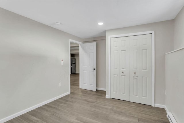 unfurnished bedroom with a baseboard heating unit, light hardwood / wood-style flooring, a closet, and stainless steel refrigerator