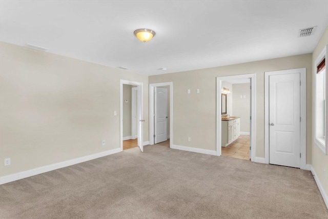 unfurnished bedroom with ensuite bathroom and light colored carpet