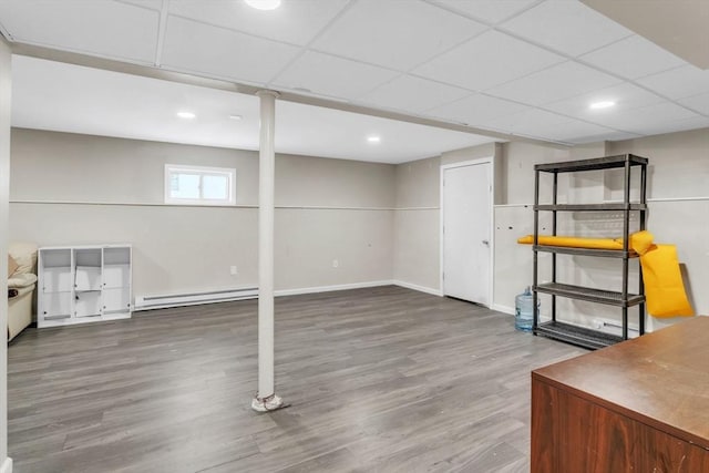 basement featuring a baseboard radiator, wood-type flooring, and a paneled ceiling