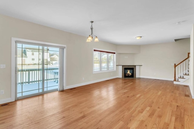 unfurnished living room with an inviting chandelier, plenty of natural light, and light hardwood / wood-style floors