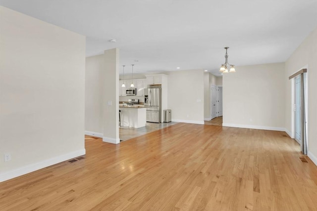 unfurnished living room with an inviting chandelier and light wood-type flooring