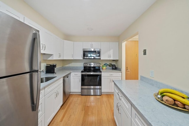 kitchen with white cabinets, sink, light hardwood / wood-style flooring, appliances with stainless steel finishes, and light stone counters