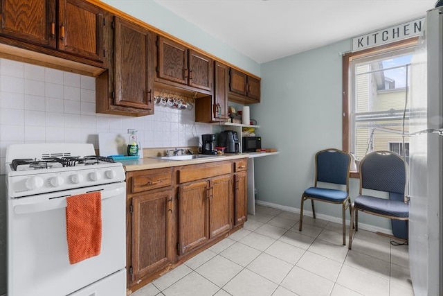 kitchen with white range with gas cooktop, light tile patterned floors, backsplash, and sink