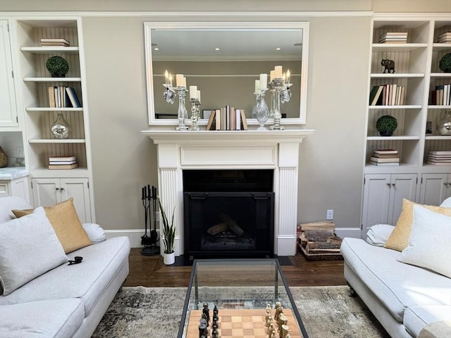 living area with dark wood finished floors, a fireplace with flush hearth, ornamental molding, and built in features