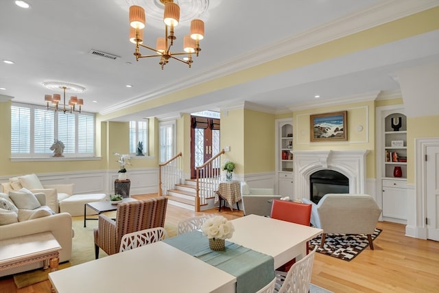 dining room with built in shelves, crown molding, light hardwood / wood-style floors, and a notable chandelier