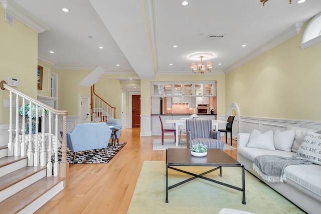 living room with ornamental molding, a notable chandelier, and light wood-type flooring