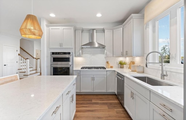 kitchen with tasteful backsplash, stainless steel appliances, sink, wall chimney range hood, and hanging light fixtures