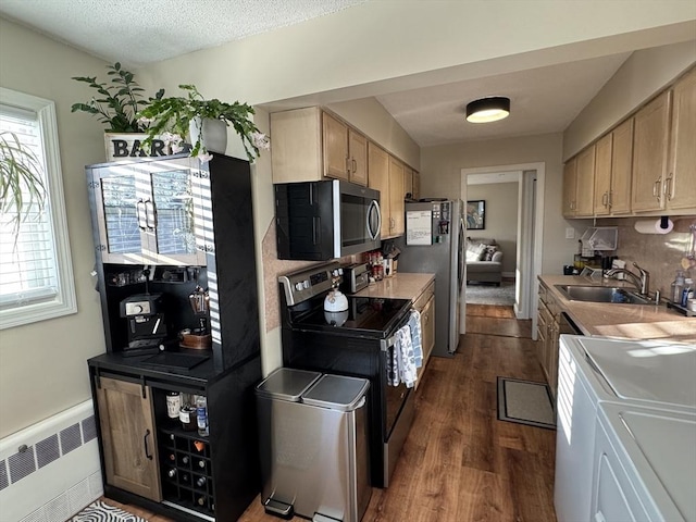 kitchen with separate washer and dryer, appliances with stainless steel finishes, radiator heating unit, dark hardwood / wood-style flooring, and sink