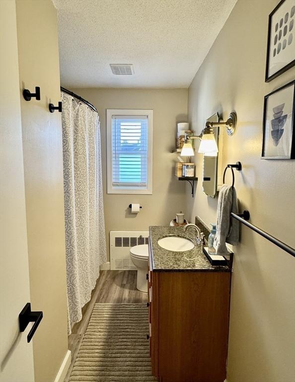 bathroom with toilet, vanity, hardwood / wood-style floors, radiator, and a textured ceiling