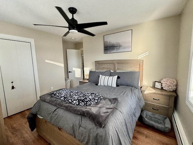 bedroom featuring ceiling fan, baseboard heating, a textured ceiling, and dark hardwood / wood-style flooring