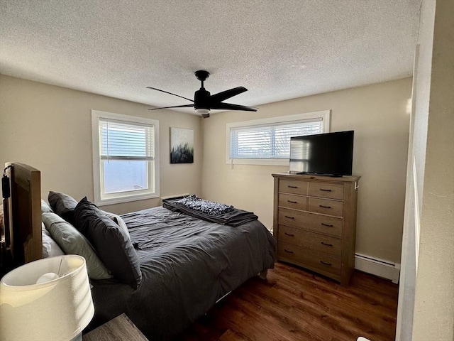 bedroom featuring ceiling fan, baseboard heating, dark hardwood / wood-style floors, and multiple windows