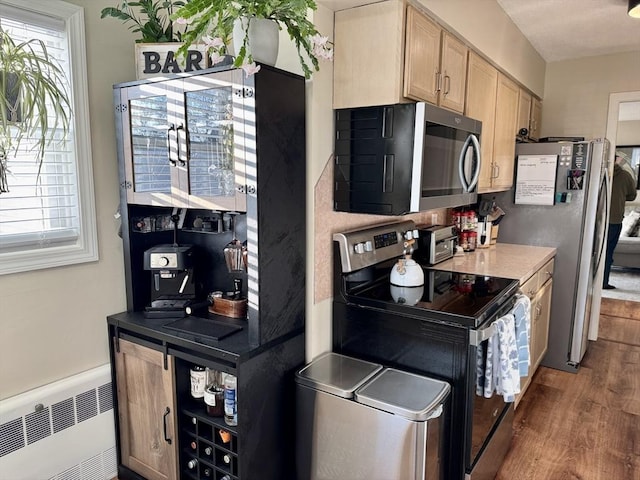 kitchen with dark wood-type flooring, radiator, appliances with stainless steel finishes, and light brown cabinets