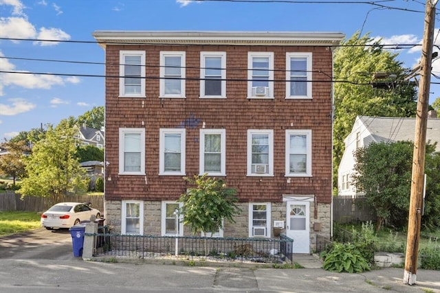 townhome / multi-family property featuring a fenced front yard, stone siding, and cooling unit