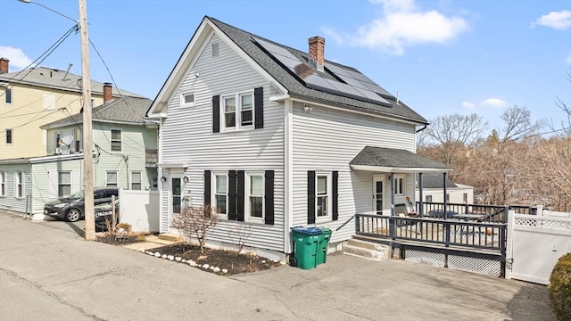 view of front of home with a wooden deck, roof mounted solar panels, a chimney, and a shingled roof