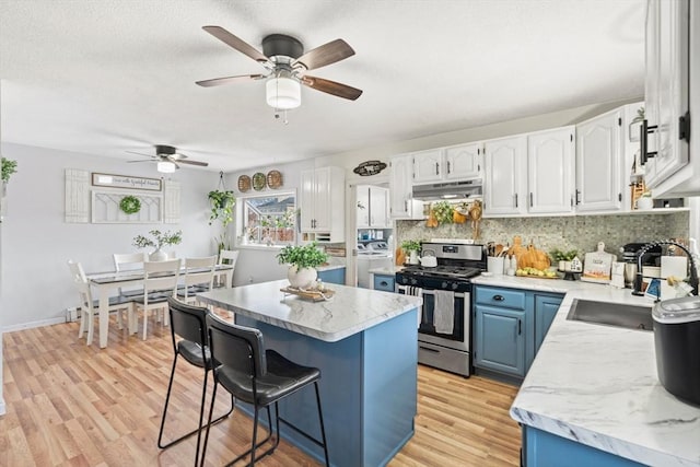 kitchen with under cabinet range hood, gas range, decorative backsplash, light wood-style floors, and blue cabinets