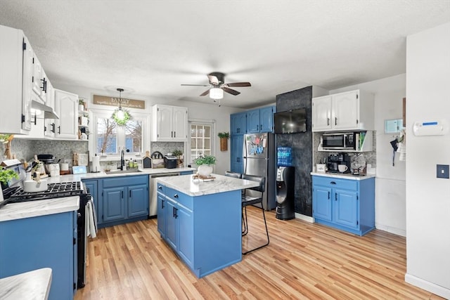 kitchen featuring blue cabinets, light wood-style flooring, under cabinet range hood, a sink, and stainless steel appliances