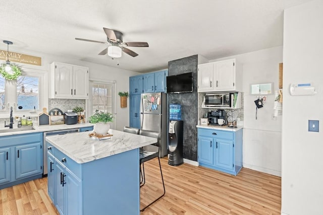 kitchen featuring blue cabinets, light wood-type flooring, a sink, appliances with stainless steel finishes, and decorative backsplash