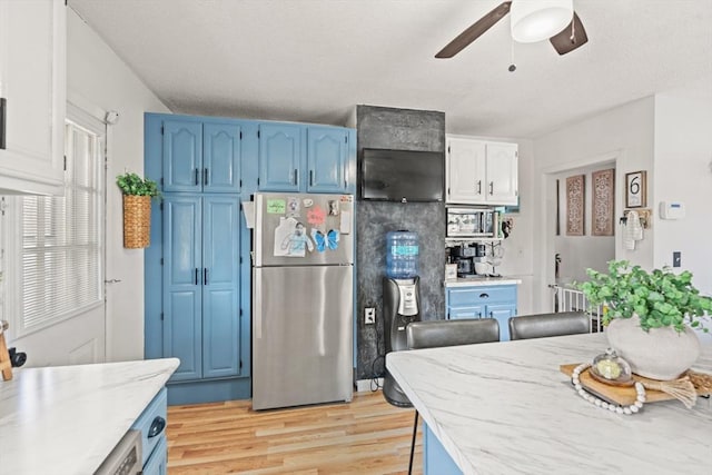 kitchen featuring blue cabinetry, ceiling fan, light stone countertops, light wood-style flooring, and freestanding refrigerator