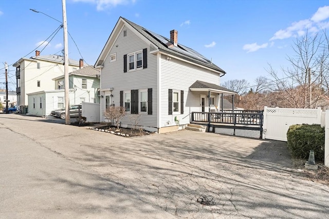 view of front of home with a porch, solar panels, a chimney, and fence