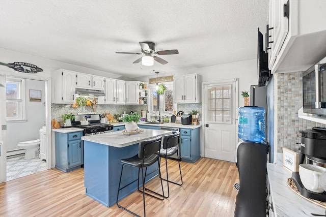 kitchen featuring gas range, blue cabinetry, light wood finished floors, and under cabinet range hood