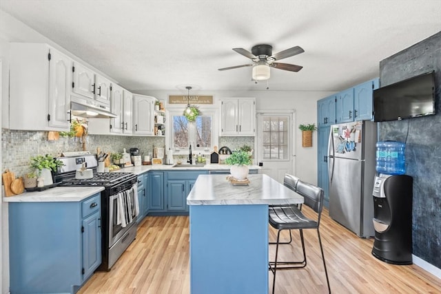 kitchen featuring blue cabinetry, a kitchen island, a breakfast bar, stainless steel appliances, and a sink